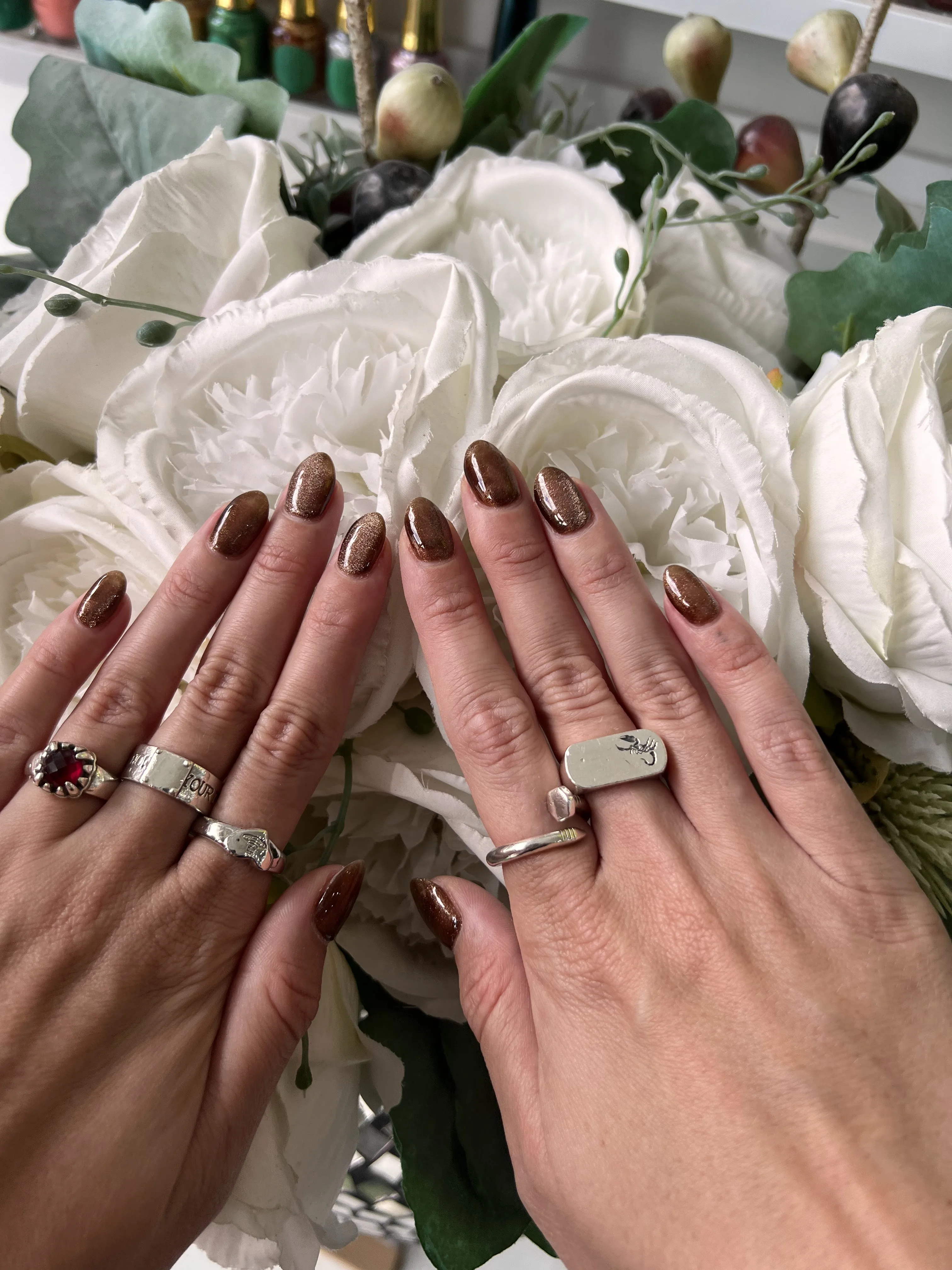 Short oval nails in a copper and bronze cat-eye shimmer with chunky silver rings