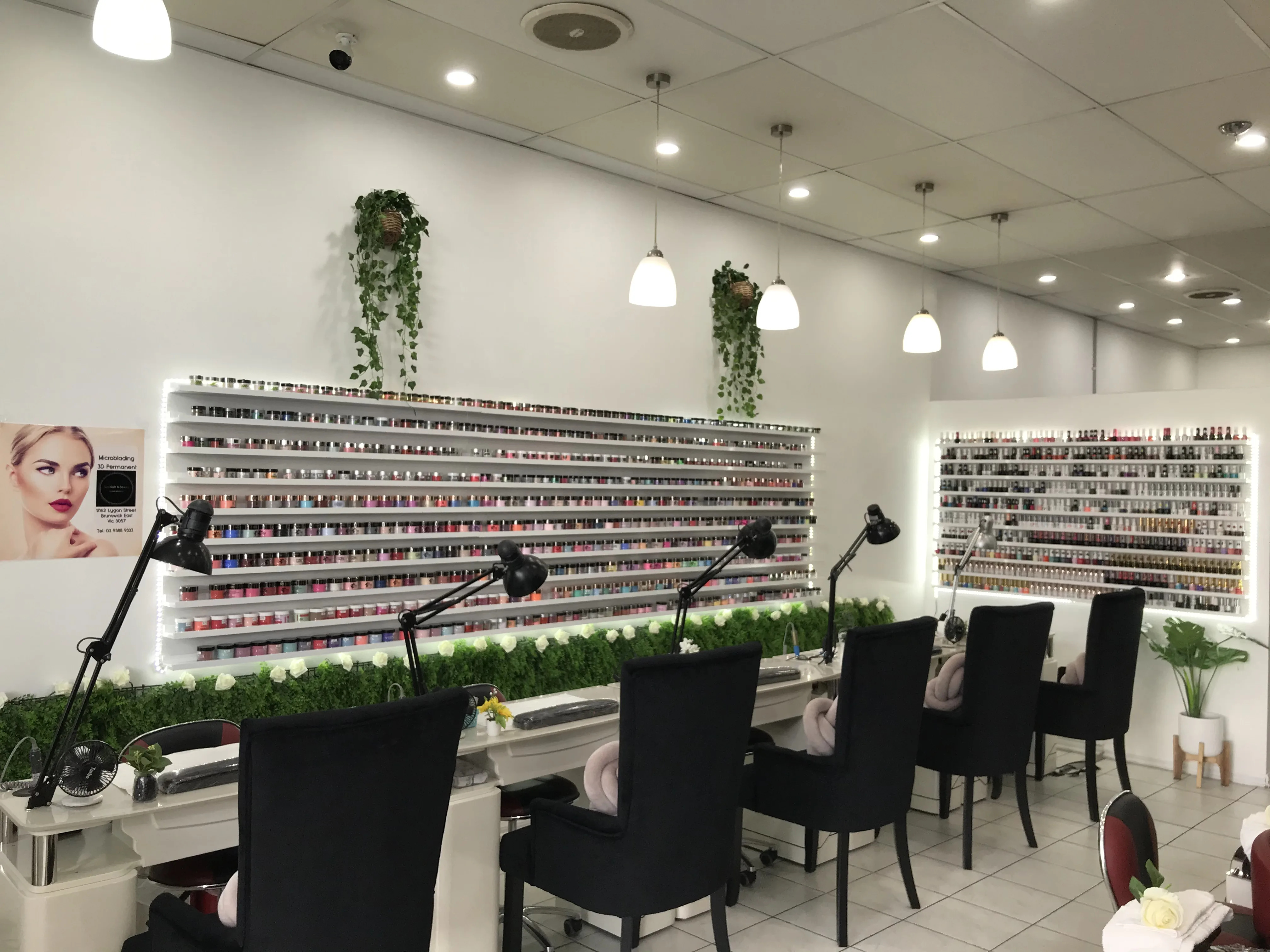 The back-lit polish wall at Sun Nails & Beauty — tiered shelves carrying hundreds of colour bottles, ivy trailing above, white roses below