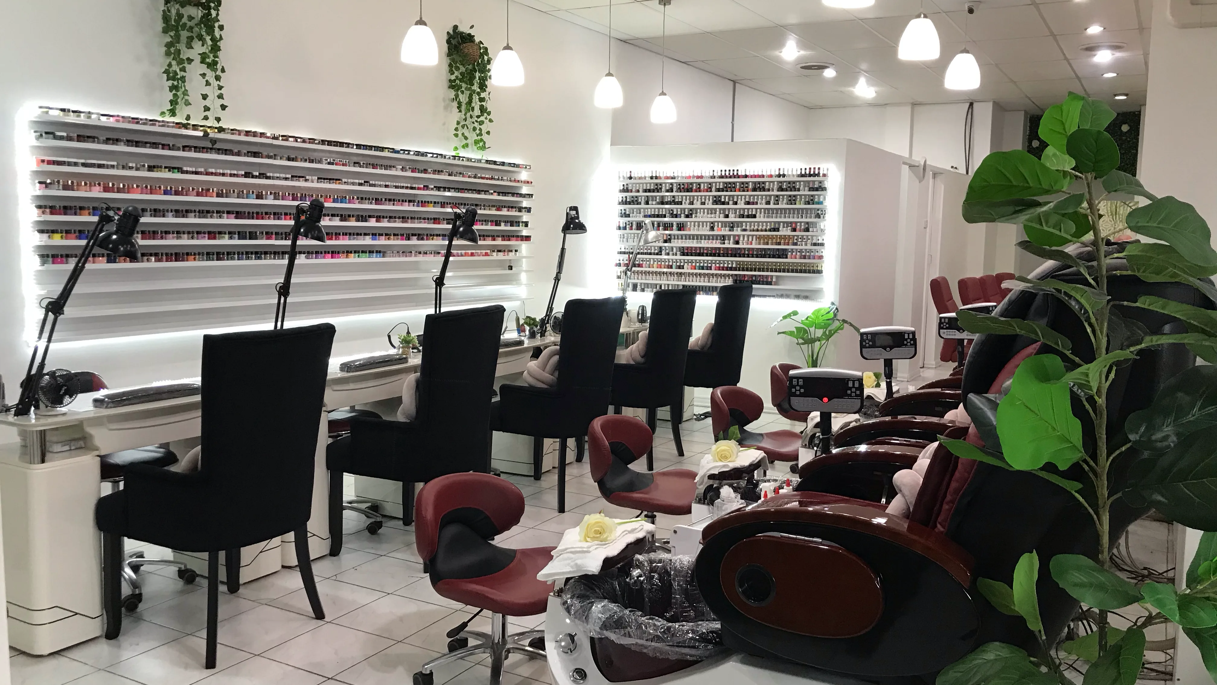 Sun Nails & Beauty interior — manicure benches and task lamps on the left, pedicure thrones on the right, two illuminated polish walls at the end