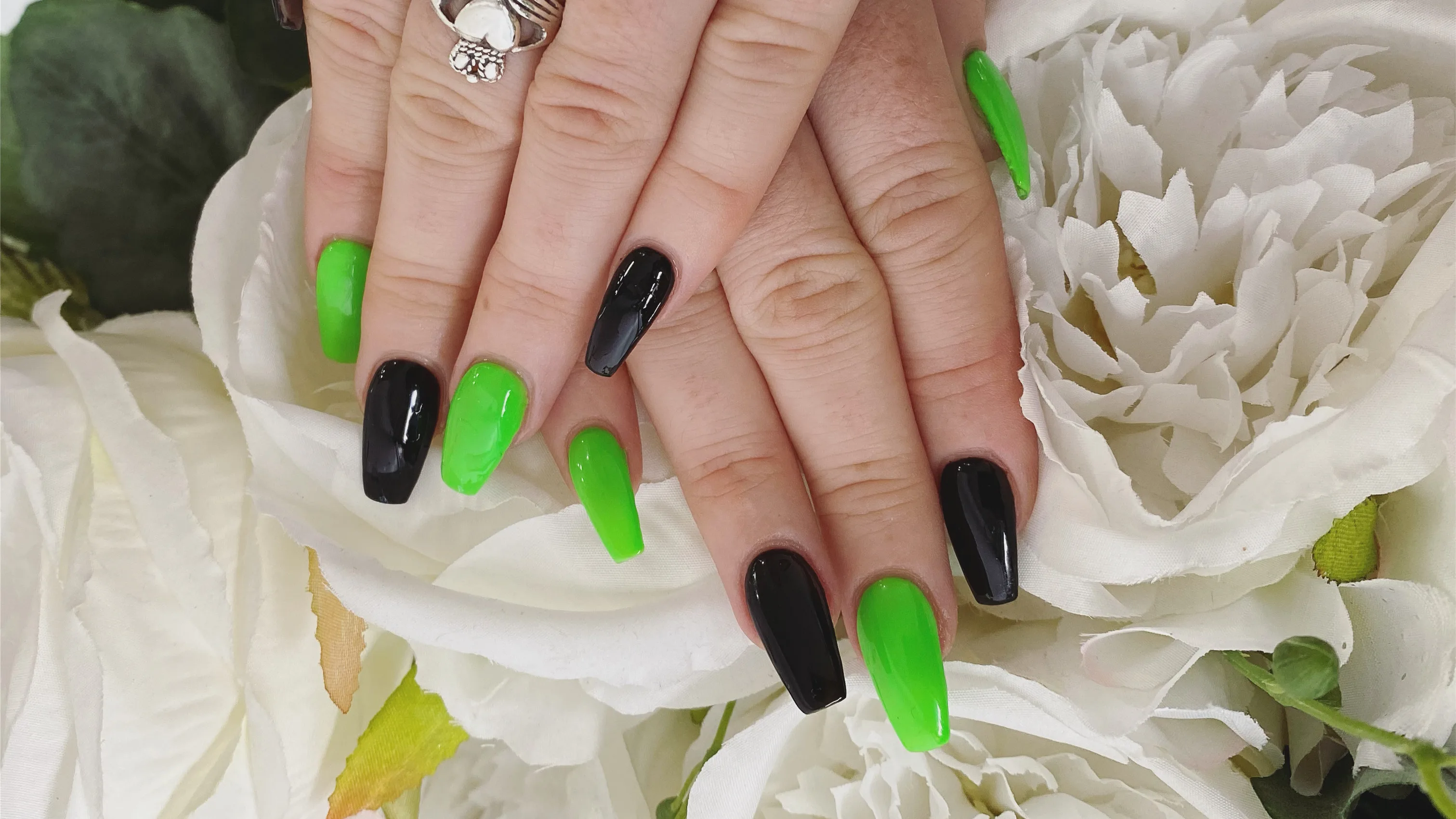 Long coffin nails alternating neon green and gloss black, hands resting on white artificial roses