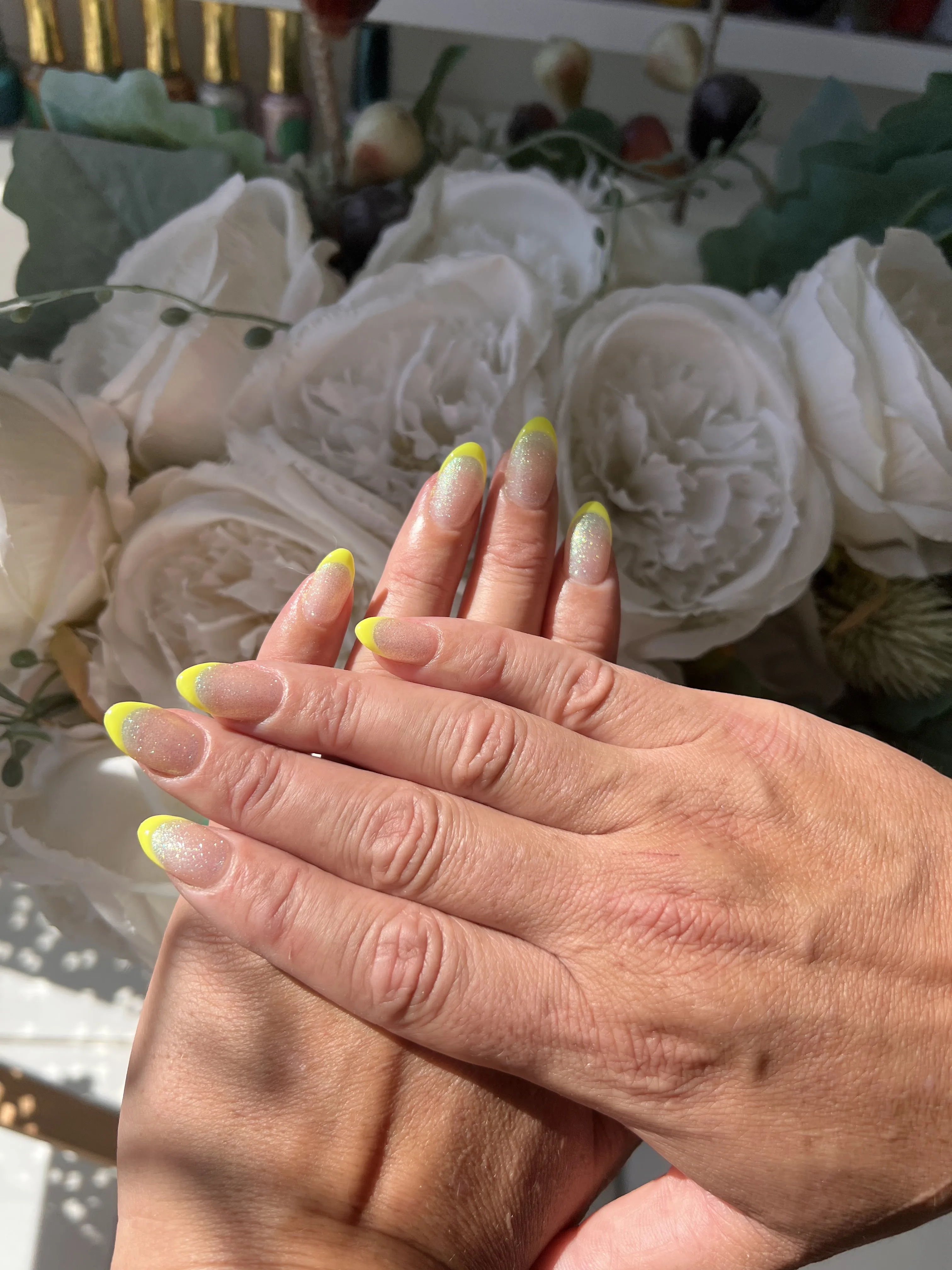 Long almond nails with an iridescent glitter base and opaque neon-yellow French tip