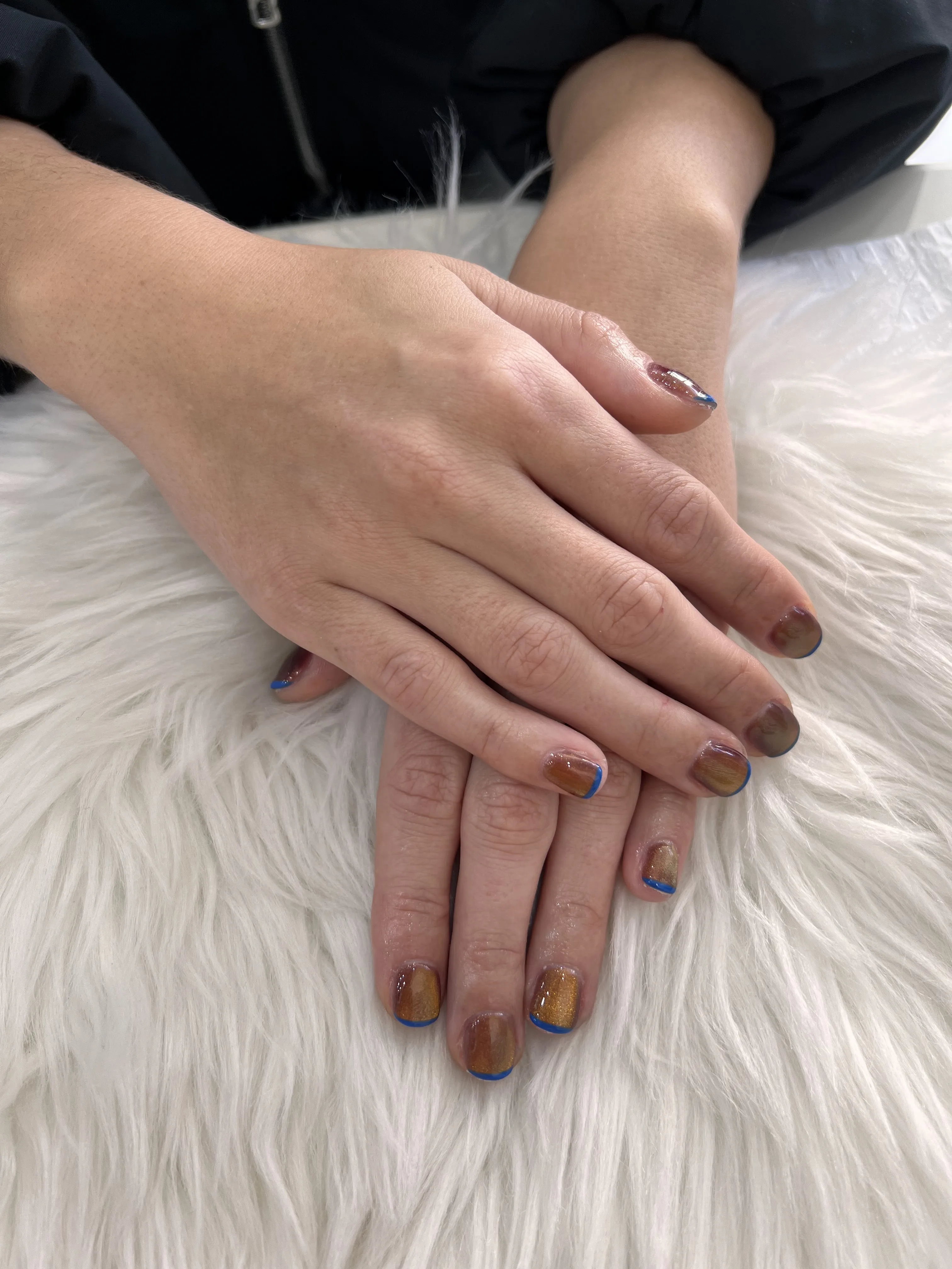 Short natural nails in a smoky brown cat-eye with a bright cobalt-blue micro French tip