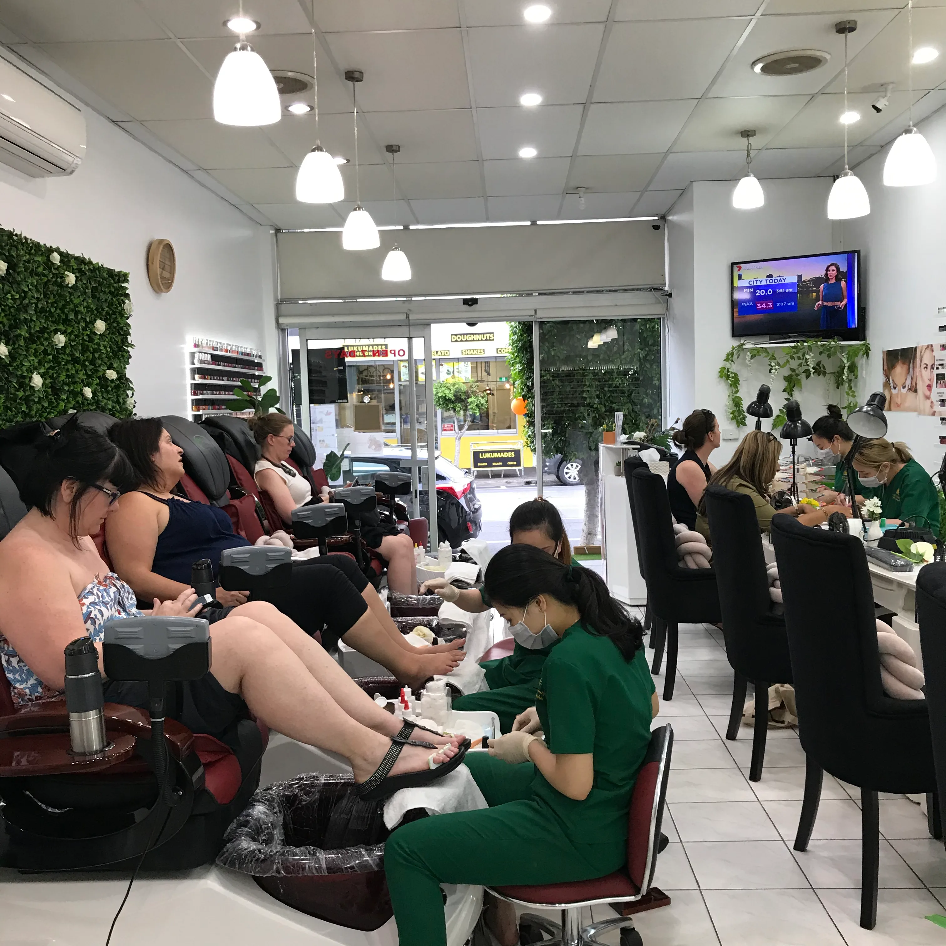 The pedicure row at Sun Nails & Beauty — clients in spa chairs with the Lygon Street window and the Lukumades doughnut shop visible through the glass
