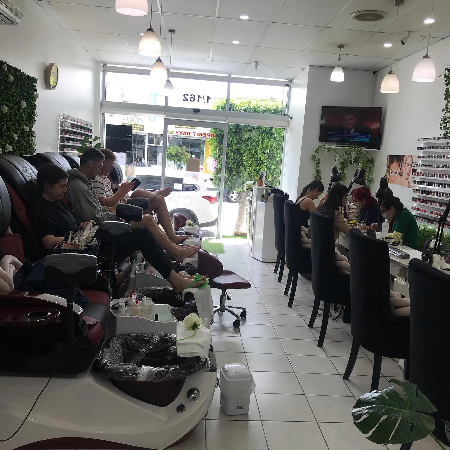 Sun Nails & Beauty from the pedicure end — the glazed shopfront with the 1/162 address read in reverse through the glass, technicians at the manicure bench
