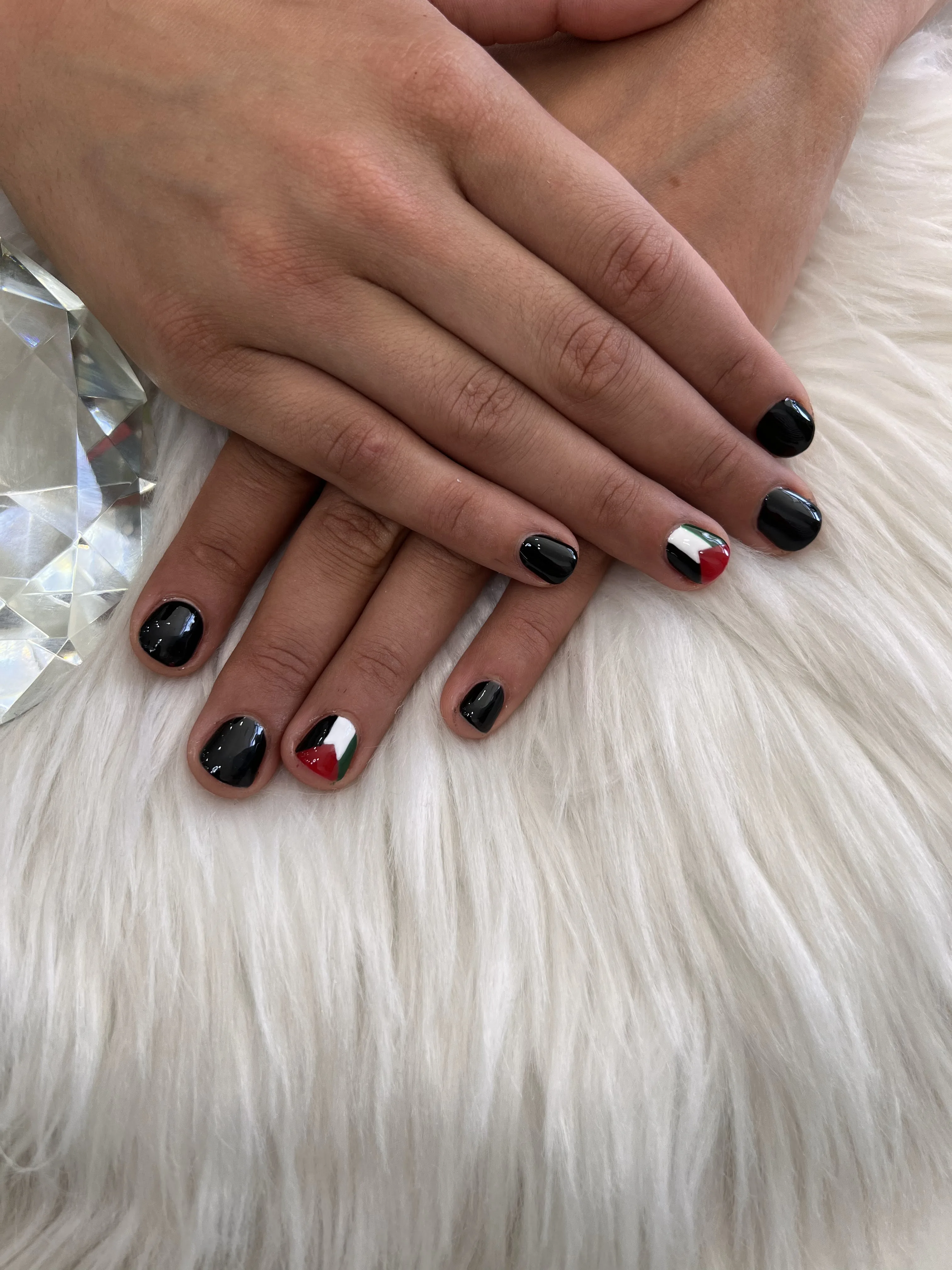Short round nails in gloss black with one accent nail, hands on white fur beside a cut-glass ornament