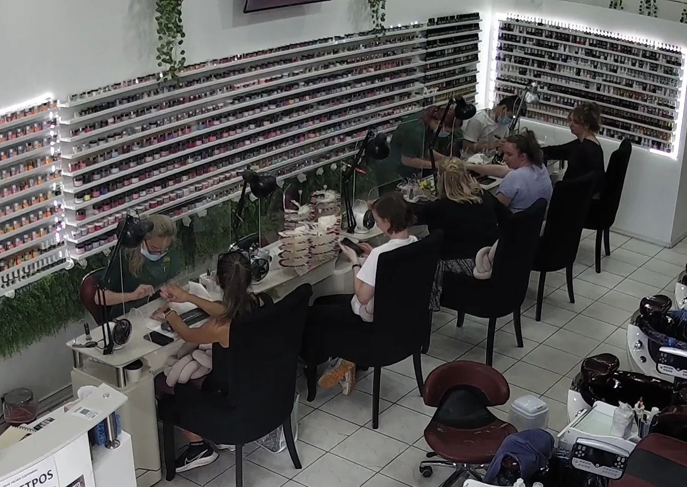 Sun Nails & Beauty at full capacity — clients at the manicure bench and pedicure chairs, technicians in forest-green uniforms working both sides
